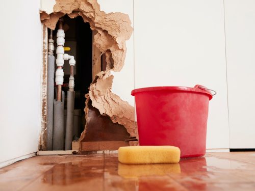 Damaged wall, exposed burst water pipes, sponge and bucket